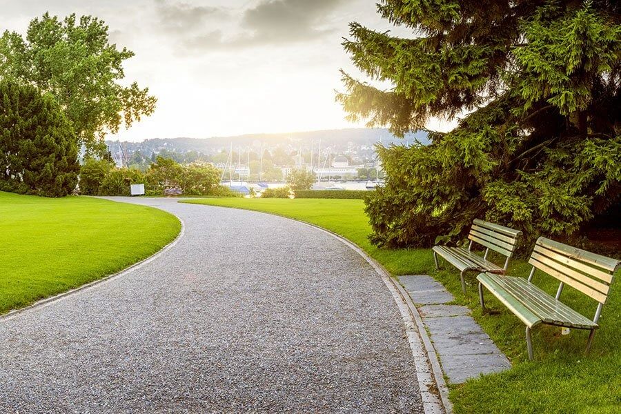 Välskött parkområde med grusväg och sittbänkar i kvällsljus – utemiljöskötsel